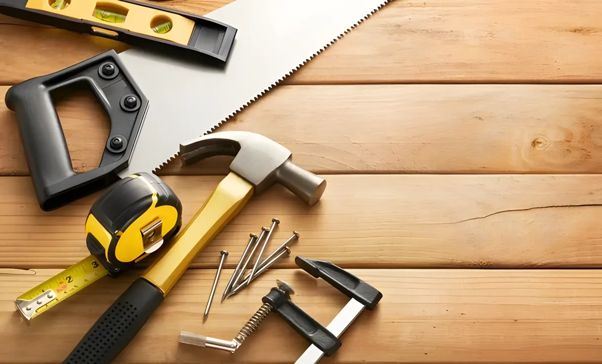 Various woodworking tools on a wooden surface, including a hammer, a tape measure, a saw, a level, nails, and clamps.