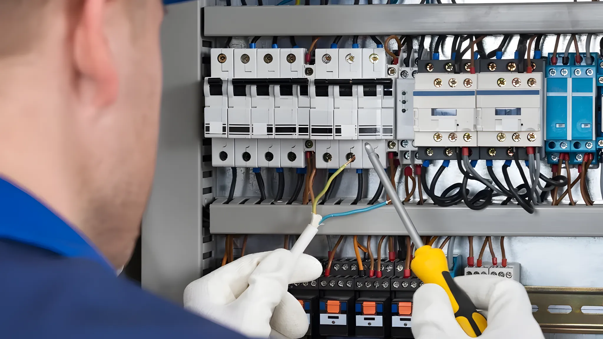 A technician working on an electrical panel, using a screwdriver and holding wires for maintenance or repair.