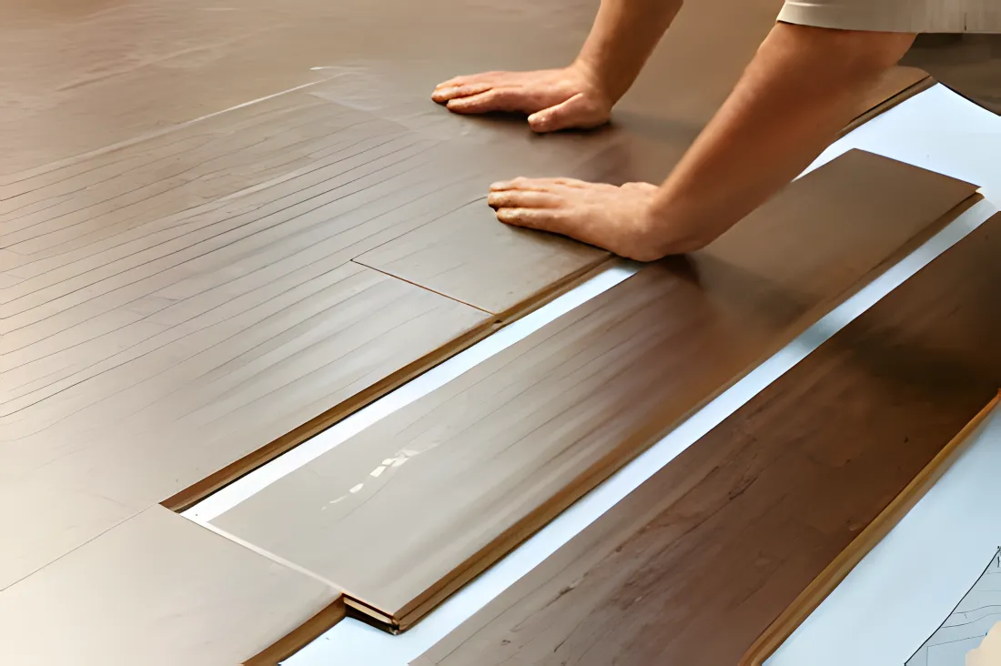 Person installing hardwood flooring on a wooden surface.